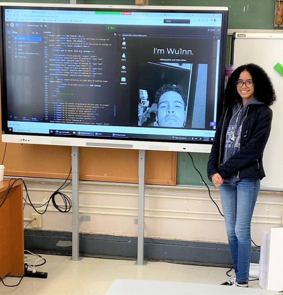 Student smiling in front of monitor filled with computer code